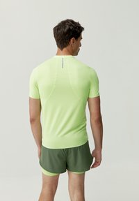Camicetta aderente a maniche corte in tessuto verde lime brillante, con un accento riflettente sulla parte posteriore, abbinata a pantaloni corti verde scuro.