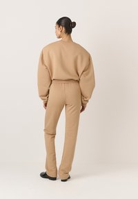 Beige, túlnőtt pulóver és azonos színű, slim-fit nadrág puha anyagból, magas derékkal és bordázott mandzsettával. Sima textúra és minimalista dizájn.