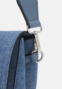 Denimväska med en strukturerad blå yta, utrustad med ett blått läderband och silverfärgade detaljer. Utmärker sig med Valentino-logotypen på spännet.