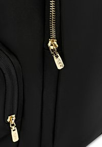 Czarny plecak z tkaniny z złotym zamkiem błyskawicznym i elementami metalowymi. Posiada gładką teksturę oraz boczną kieszeń z detalem metalowego uchwytu zamka.