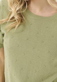 Ljusgrön stickad tröja med korta ärmar, med strukturerade bobbledetaljer och en ribbad halsringning. Mjuk, slät material.