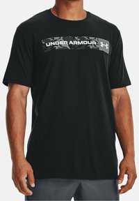 T-shirt nero a maniche corte realizzato in cotone. Presenta un motivo mimetico con "UNDER ARMOUR" in bianco sulla parte anteriore e il logo sul lato.
