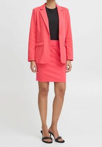 Korallfärgad blazer med två framfickor över en svart ribbad topp, parat med en korallfärgad penkjol och svarta klacksandaler.