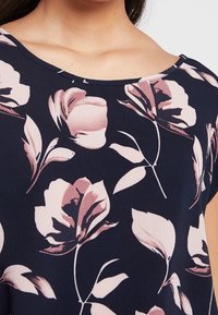 Blusa floreale blu navy con scollo rotondo, maniche corte e un motivo di fiori e foglie rosa chiaro su un tessuto liscio.