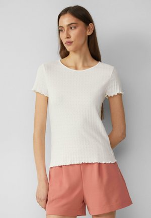 Weißes gestreiftes T-Shirt mit kurzen, gewellten Ärmeln, rundem Halsausschnitt und strukturiertem Muster; kombiniert mit rosa Shorts.