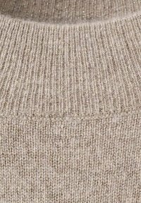 Acercamiento de un suéter de punto color beige, con textura acanalada y acentos de hilos metálicos, que destaca su apariencia suave y acogedora.