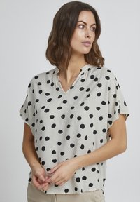 Blusa leggera e trasparente con scollatura a V; tessuto crema decorato con grandi pois neri; vestibilità comoda; maniche corte; finitura testurizzata.