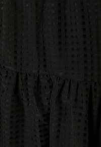 Robe noire avec un motif texturé de petits carrés, présentant des détails froncés au niveau de l'ourlet. Tissu doux et léger.