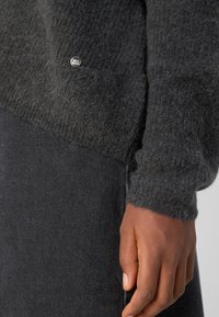 Dunkelgrauer gestrickter Pullover mit flauschiger Textur und Bündchenärmeln, mit einem silbernen MOS MOSH-Logo auf der Vorderseite.