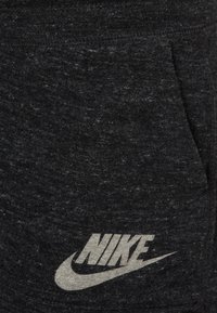 Černá pletená mikina s kapucí a přední kapsou, která se pyšní výrazným šedým logem Nike. Textura je měkká a má jemné variace.