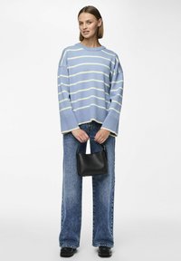 Ljusblå rutig tröja med breda ärmar, parat med högmidjade urtvättade blå jeans och en liten svart handväska. Texturerat stickat tyg.