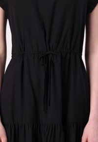 Zwart jurkje gemaakt van lichtgewicht stof, met een cinched taille met een trekkoord en een gelaagd rokje. Korte mouwen, eenvoudige stijl.