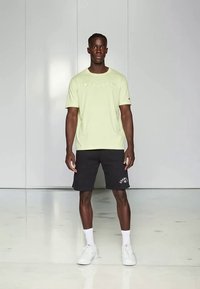 Heleroheline lühikeste varrukatega t-särk, millel on rinna kohal "Champion" logo, koos mustade lühikestega, millel on valge "G" logo, kantud valgete tossudega.