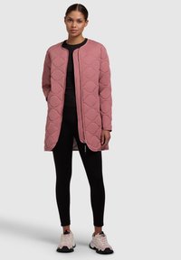 Manteau matelassé rose clair avec un col rond, fermeture éclair sur le devant et motif texturé. Associé à des leggings noirs et des baskets blanches.