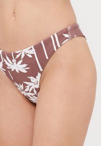 rudas bikini kelnaitės su baltu gėlių raštu ir vertikaliomis juostelėmis. Pagamintos iš tamprių medžiagų, minimalistinio dizaino.
