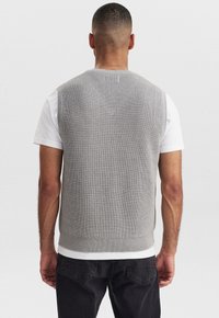 Grauer Strickwesten mit gerippter Textur, rundem Ausschnitt und tailliertem Saum, getragen über einem weißen T-Shirt. Von hinten gesehen, ohne Muster oder Akzente.