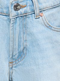 Jean en denim bleu clair en gros plan montrant un bouton, une passants de ceinture, une poche avant et des coutures orange contrastées.