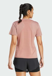 Kortärmad, lätt atletisk tröja i blushrosa med en mjuk yta, som har kontrasterande sömmar och en avslappnad passform, i kombination med svarta shorts.