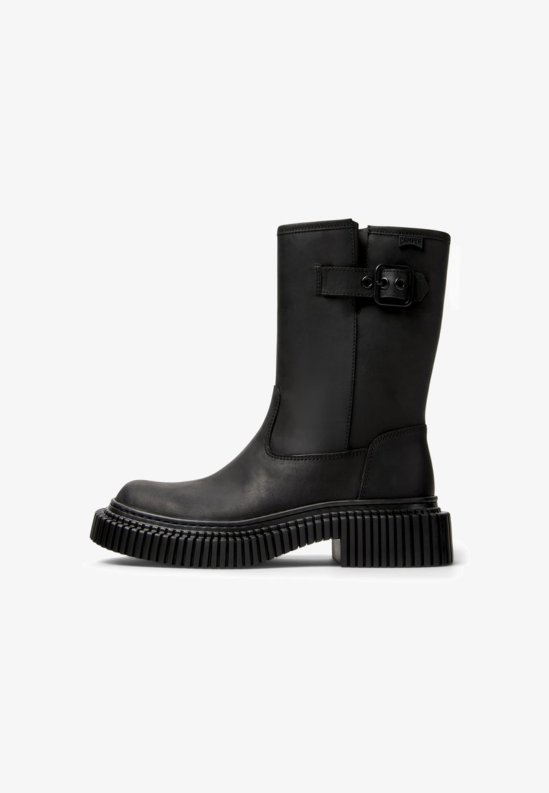 Černá kožená kotníková bota se zaoblenou špičkou, širokým páskem a detailním přezkovým zapínáním a silnou, drsnou gumovou podrážkou pro lepší přilnavost.