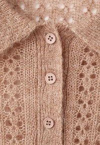 Cárdigan de punto en suave beige con un patrón de encaje texturizado y botones lisos y brillantes. Presenta un cuello con solapa y detalles de diseño delicados.