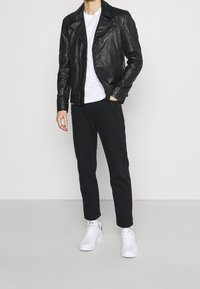 Zwarte leren bikerjack met ritstassen, gedragen over een wit T-shirt, gecombineerd met zwarte broek en witte sneakers. Eenvoudig, modern ontwerp.