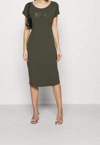 Oliivivärvi midi-kleid, jossa on lyhyet hihat, ja brändin nimi "LIU JO" kohokuvioituna. Hopeiset nauhakengät.