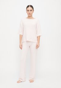 Σετ ροζ λευκής άνετης ρουχισμού από μαλακό ύφασμα, που περιλαμβάνει ένα λοξό κοντομάνικο τοπ σε χαλαρή γραμμή και παντελόνια με φαρδιά πόδια και λεία υφή.
