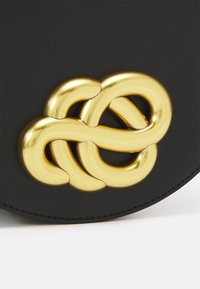 Geantă din piele neagră cu un închizător mare, împletit din metal auriu. Designul include curbe fine și accente lustruite.