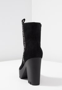 Czarne botki za kostkę z sztucznego zamszu na grubej podeszwie. Posiadają elastyczny pasek z nadrukowanym logo z tyłu oraz gładką gumową podeszwę.