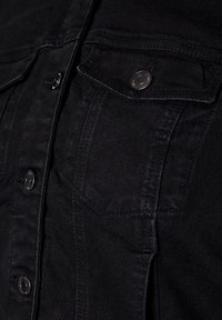 Close-up van de voorzak van een zwarte denim jas met metalen drukknoopjes en gedetailleerde stiksels op de dikke stof.