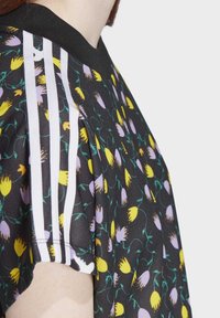 Černé květinové tričko s žlutými a purpurovými květy, s jemně vroubkovaným černým límcem a třemi bílými pruhy na rameni.