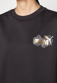 Sweat-shirt noir à encolure ronde, orné d'une broderie florale et d'un logo métallique en or et blanc sur le côté gauche. Texture douce.