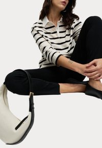 Polo à manches longues rayé avec un col blanc, pantalon noir slim fit et sac crème avec des accents noirs et une fermeture éclair dorée.