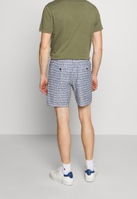 Pantalones cortos de tela estampada con motivos en gris y blanco, con un frente plano, dos bolsillos en la parte posterior y un ajuste cómodo. Combinados con una camiseta verde.