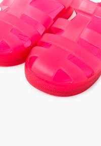Pink plastic sandals with a strappy design, featuring open-toe construction and textured soles for grip. Lightweight and flexible material.
