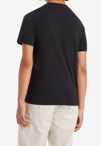 Černé tričko s krátkým rukávem a klasickým kulatým výstřihem. Vyrobeno z hladké látky; na levém švu se nachází logo štítek. Jednoduchý, minimalistický design.