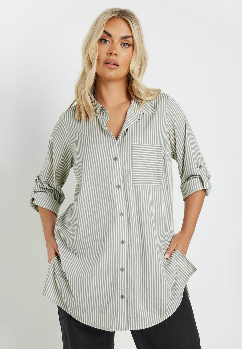 Camicia a righe verde chiaro e bianca. Presenta una tasca sul petto, maniche arrotolabili e un orlo looser e curvato.