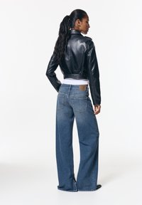 Čierna kožená skrátená bunda s pásom, doplnená širokými džínsami modrej farby s vreckami na zadnej strane a detailom záplaty.