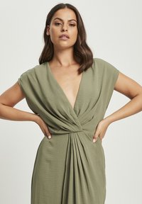 Olive green dress with a deep V-neck and pleated design. Loose, cap sleeves and smooth, textured fabric.