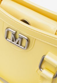 Geel gepatenteerd leren handtas met een zilveren metalen logo en gespaccenten, met een gladde textuur en een compacte rechthoekige vorm.