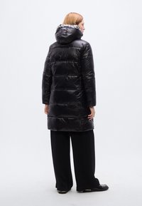 Μαύρο μπουφάν τύπου puffer με γυαλιστερό φινίρισμα, κουκούλα και λευκό λογότυπο σε αντίθεση στον εσωτερικό γιακά. Διαθέτει ραμμένες ενότητες και μεσαίο μήκος.