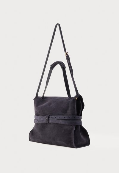 Sac à bandoulière en daim noir avec une sangle réglable, un détail ceinture autour du milieu et deux poignées plus courtes, présenté sur un fond clair uni.