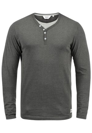 Camicia a maniche lunghe di colore grigio scuro, realizzata in tessuto morbido, con scollatura henley dotata di tre bottoni e colletto interno di un grigio chiaro a contrasto.