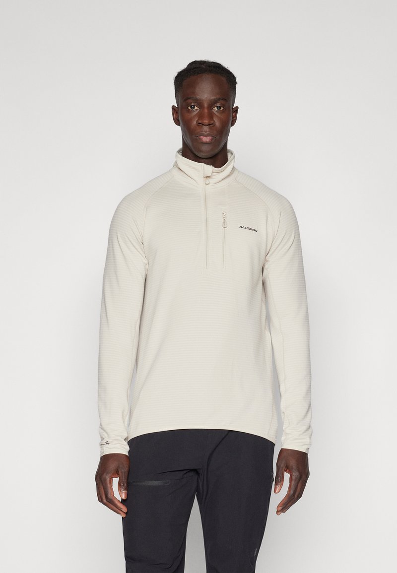 Pullover a mezzo zip di colore beige chiaro con tessuto testurizzato, maniche lunghe e colletto alto. Presenta un piccolo logo sul petto e una tasca con zip.
