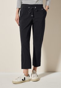 Zwarte, lichte, cropped joggerbroeken met een elastische tailleband en trekkoord. Gepaarde met witte sneakers met zwarte accenten.
