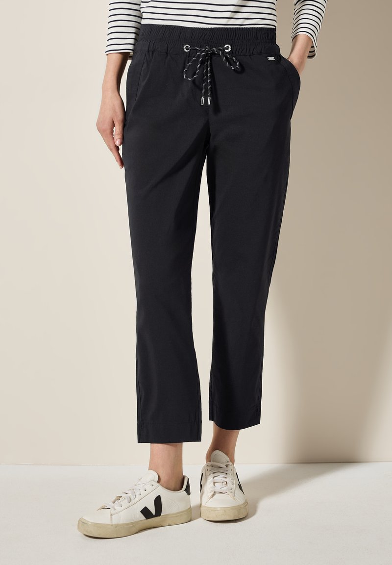 Zwarte, lichte, cropped joggerbroeken met een elastische tailleband en trekkoord. Gepaarde met witte sneakers met zwarte accenten.