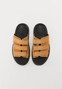 Sandali in suede beige con tre cinturini regolabili; suola in gomma nera con cuciture arancioni; design piatto, punta e tallone scoperti.