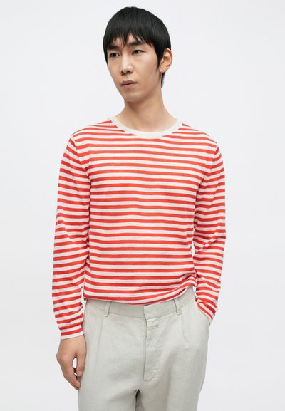 Chemise à manches longues rayée rouge et blanche avec un col rond, en tissu doux. Associée à un pantalon clair, ajusté et confectionné sur mesure.