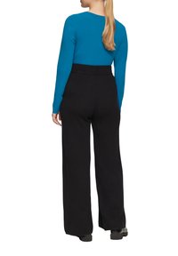 Turquoise lange mouwen top gecombineerd met hoge taille zwarte broek, heeft een wijd been ontwerp en een gladde textuur, gezien vanaf de achterkant.