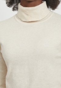 Maglione beige a collo alto realizzato in morbido tessuto a maglia, con un colletto a coste e una texture liscia, caratterizzato da una silhouette aderente.